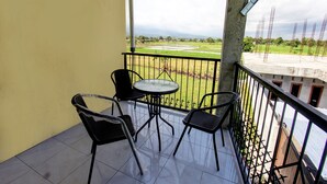 A balcony with a table and chairs, offering a view of a green landscape and distant buildings.