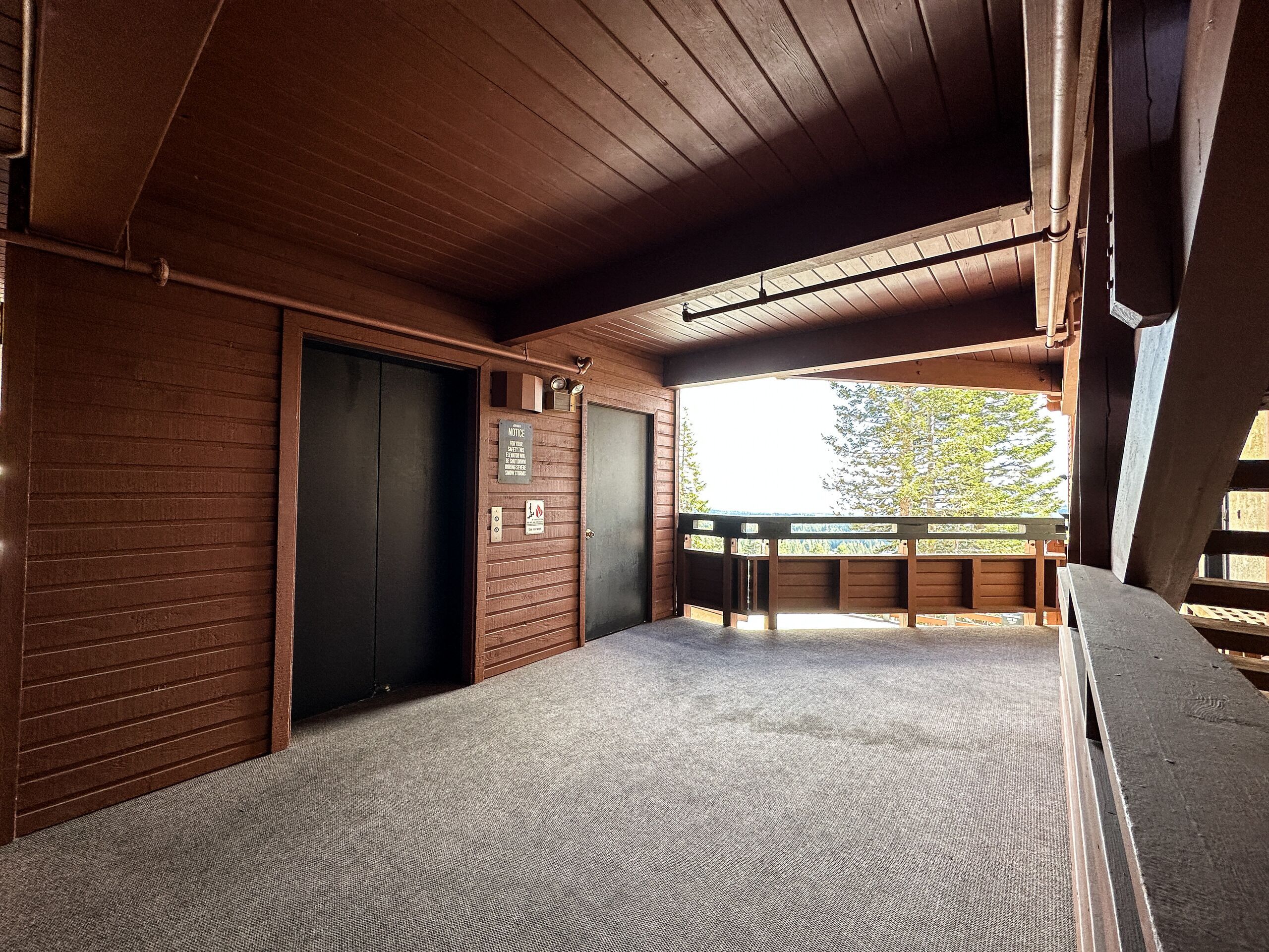 A wooden interior with a carpeted floor, a door, and a window overlooking a deck area.