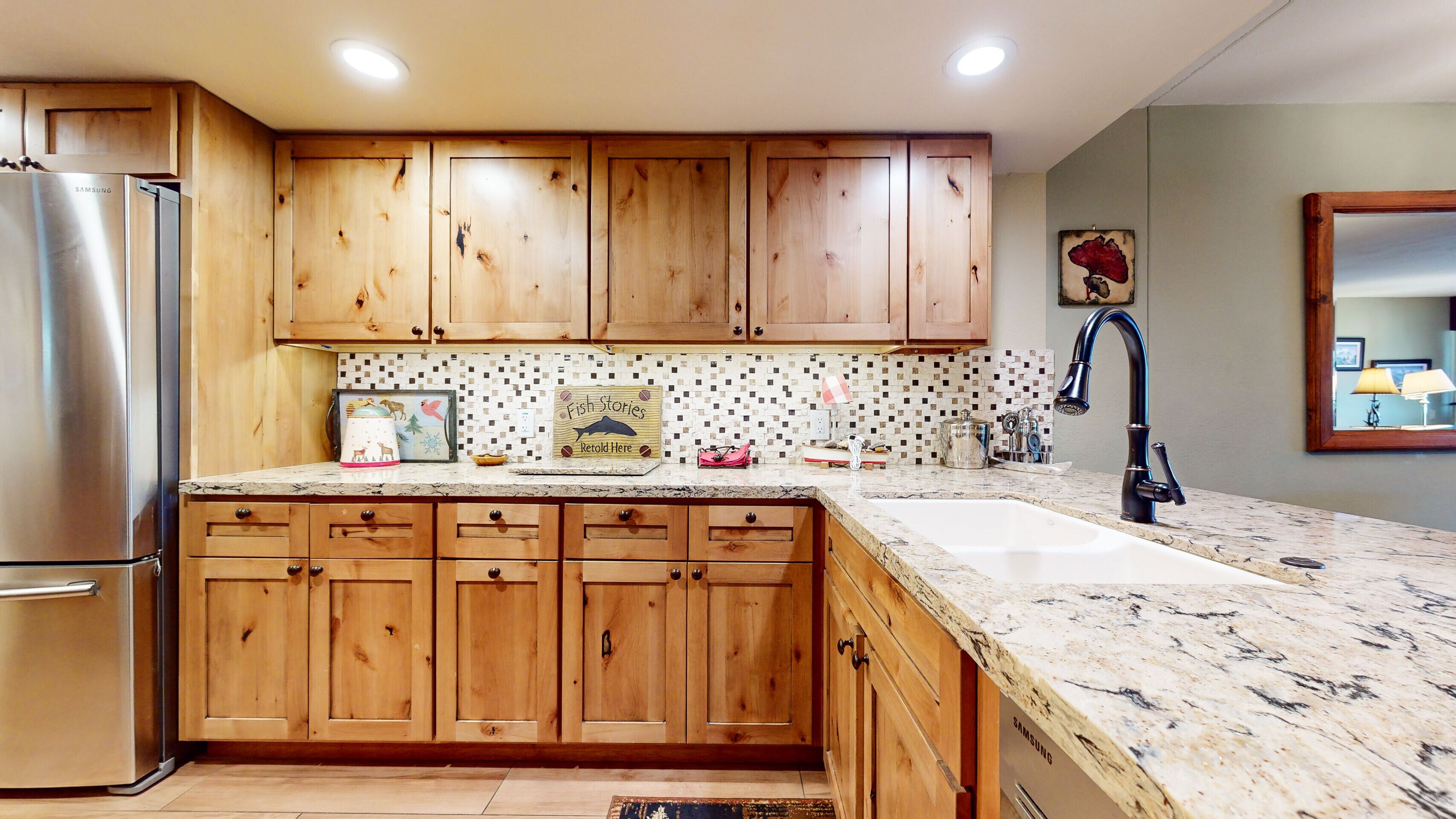 A kitchen with wooden cabinets, a stainless steel refrigerator, a marble countertop, and a sink.