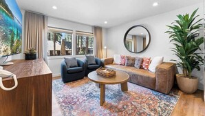 Een moderne woonkamer met een bank, twee fauteuils, een salontafel, een grote spiegel en een kamerplant.