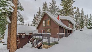 Eine Holzhütte mit einer Treppe zu einer Terrasse, umgeben von schneebedeckten Bäumen.
