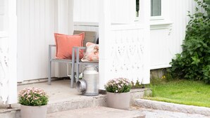 A white building with a porch, a chair, and two potted plants. - Trugstad Gård (Nannestad)