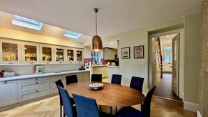 A modern kitchen with a wooden dining table, blue chairs, and a pendant light. - Stunning Family Home in Tulse Hill (London)