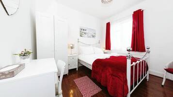 A bedroom with a white bed, red curtains, a white dresser, and a red patterned rug.
