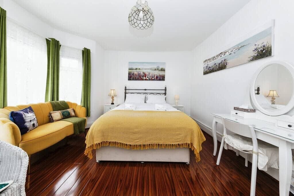 Een slaapkamer met een bed, een bureau, een stoel, een spiegel en een schilderij aan de muur.