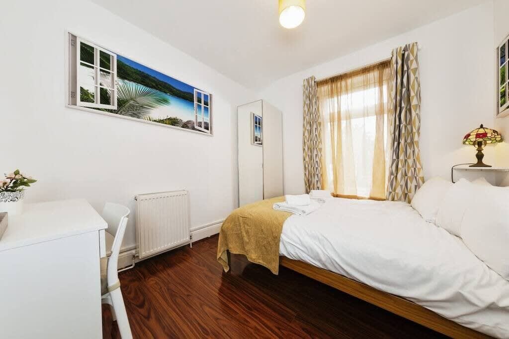 A bedroom with a bed, a desk, a radiator, and a window with curtains.