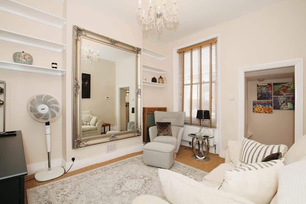 A living room with a large mirror, a fan, a sofa, and a window with blinds.