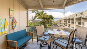 A covered outdoor seating area with a table and chairs, a blue sofa, and a view of a residential building and palm trees.