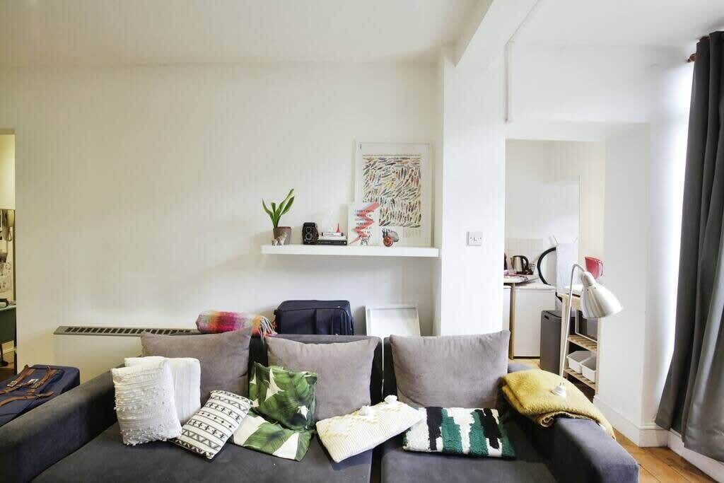 Un salon moderne avec un canapé gris, une petite plante et une étagère ornée d’objets décoratifs.