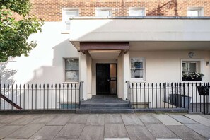 A townhouse with a front entrance, a small porch, and a brick building in the background.