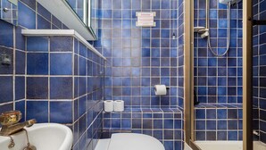Un baño con paredes de azulejos azules, un lavamanos blanco, un inodoro y una zona de ducha.