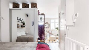 Una camera da letto moderna con un letto, un armadio, un piccolo angolo relax e vista sul soggiorno.