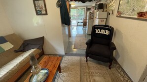 Un espace de vie compact comprenant un canapé, une petite table avec un verre et une chaise portant l’étiquette « COMBO ». On aperçoit un réfrigérateur et un coin repas à l’arrière-plan.