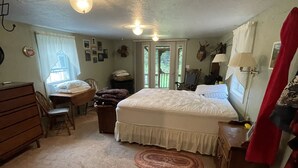 Une chambre à coucher comprenant un lit, un bureau, une chaise, une commode et une porte donnant sur l’extérieur.