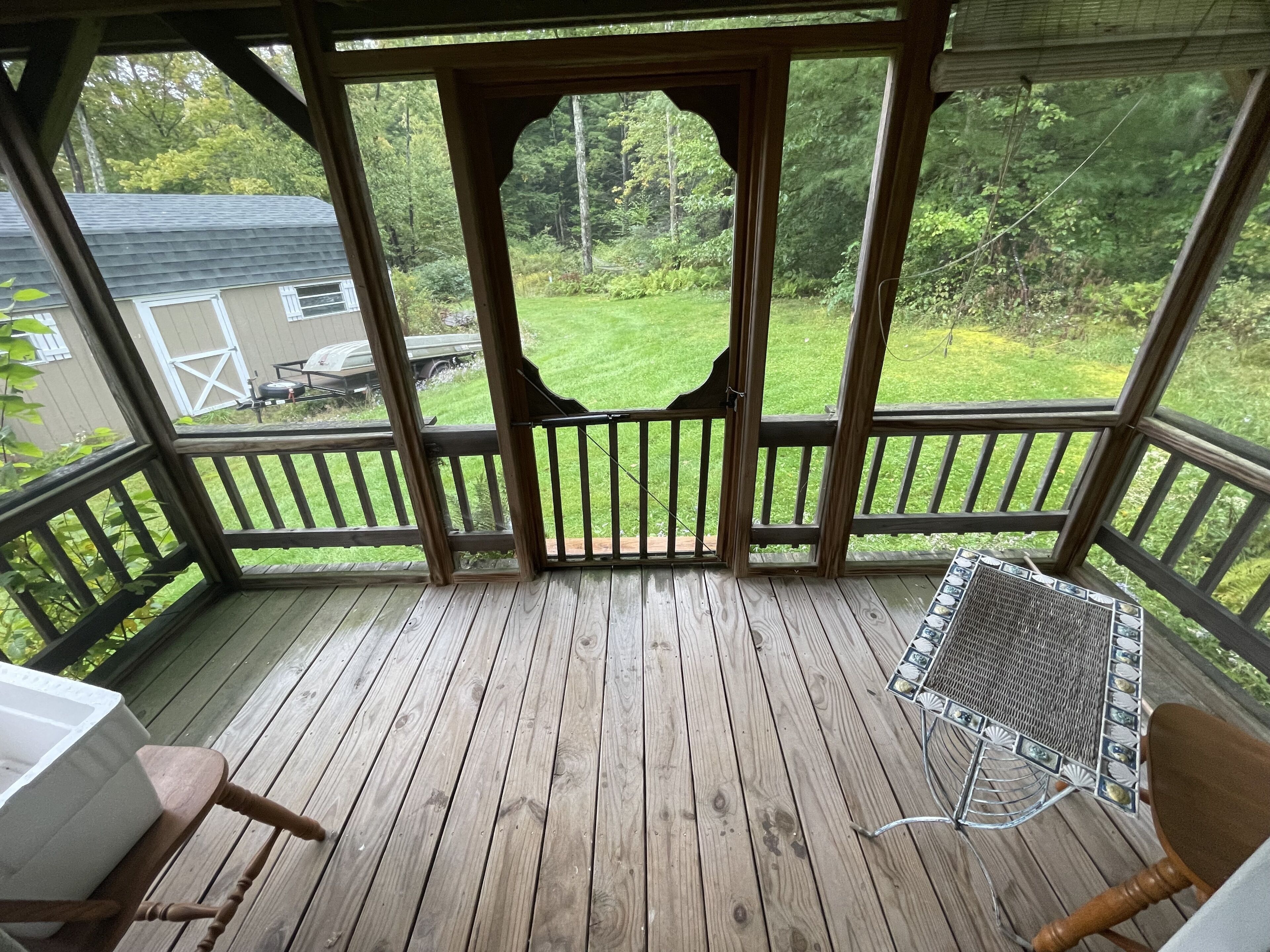 A wooden deck with a covered seating area, a grill, and a view of a green yard.