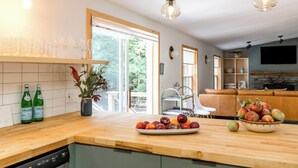 Una cocina con encimera de madera, un rincón comedor con sofá de cuero y una chimenea de piedra.