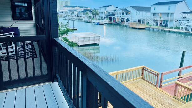 A wooden deck with a view of a marina and houses across the water. - Waterfront Beach House on the Canal with Deep Water Access to Ocean w/Boat Ramp. (North Myrtle Beach)