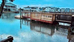 A waterfront property with a wooden dock and a house with a balcony. - Waterfront Beach House on the Canal with Deep Water Access to Ocean w/Boat Ramp. (North Myrtle Beach)