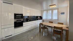 A modern kitchen with white cabinets, a black countertop, and a dining area with a wooden table and chairs. - Place to relax  (Zermatt)
