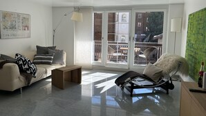 A modern living room with a sofa, a lounge chair, a coffee table, and a view through large windows to an outdoor balcony. - Place to relax  (Zermatt)