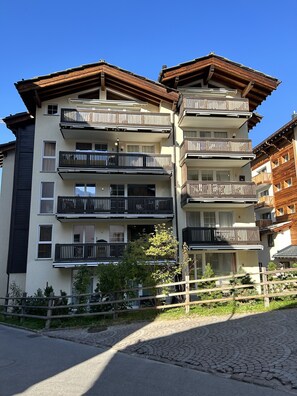 Un immeuble à plusieurs étages doté de balcons, d’une allée pavée et d’un petit jardin.