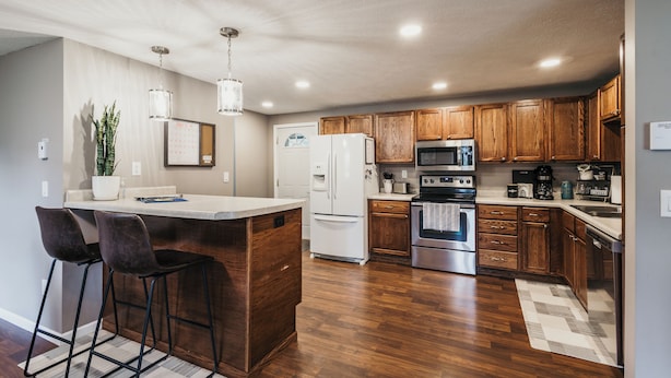 A modern kitchen with wooden cabinets, stainless steel appliances, and a bar area with stools.