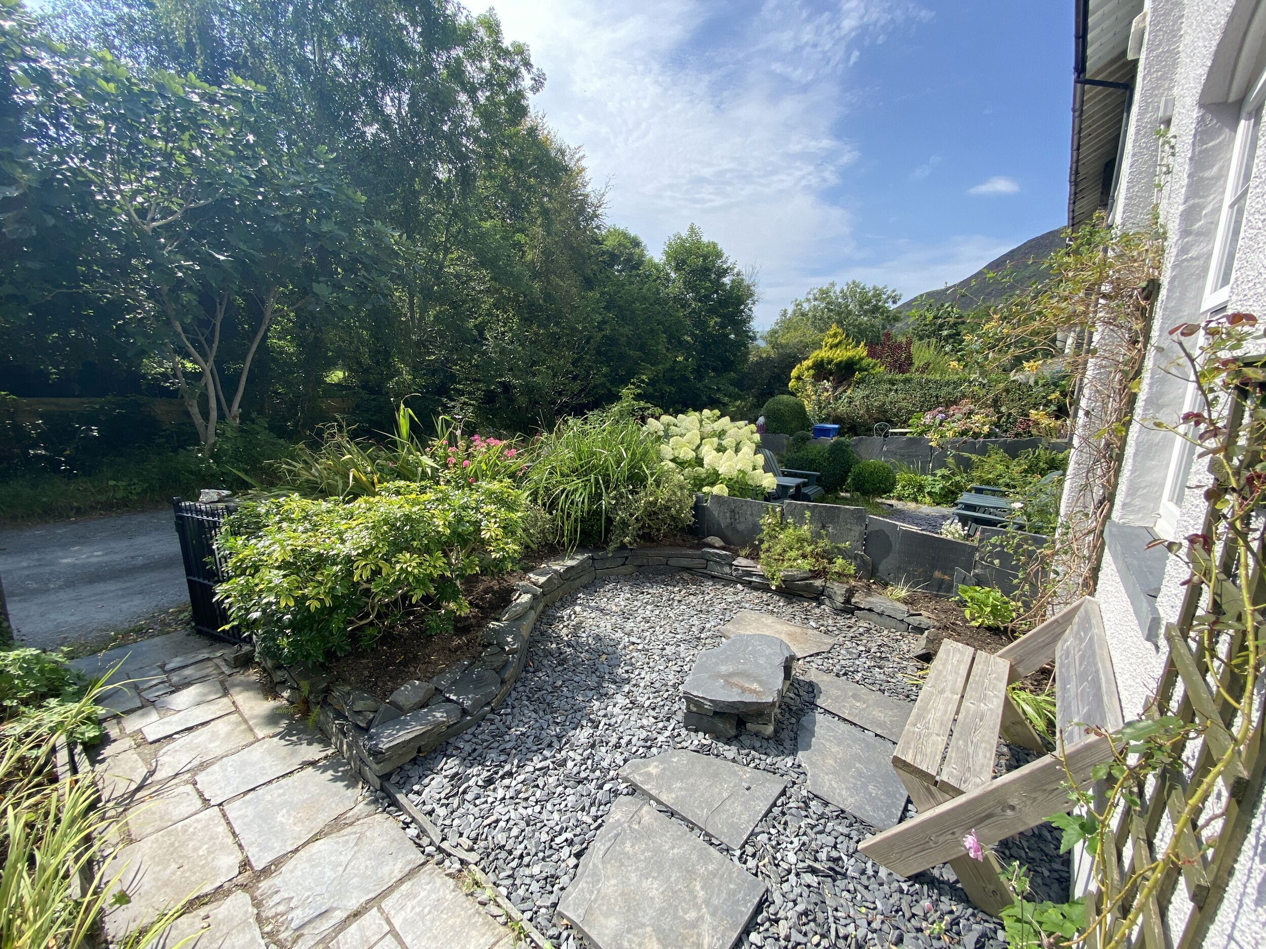 Ein Garten mit einem Kiesweg, einer kleinen Sitzgelegenheit und verschiedenen Pflanzen.