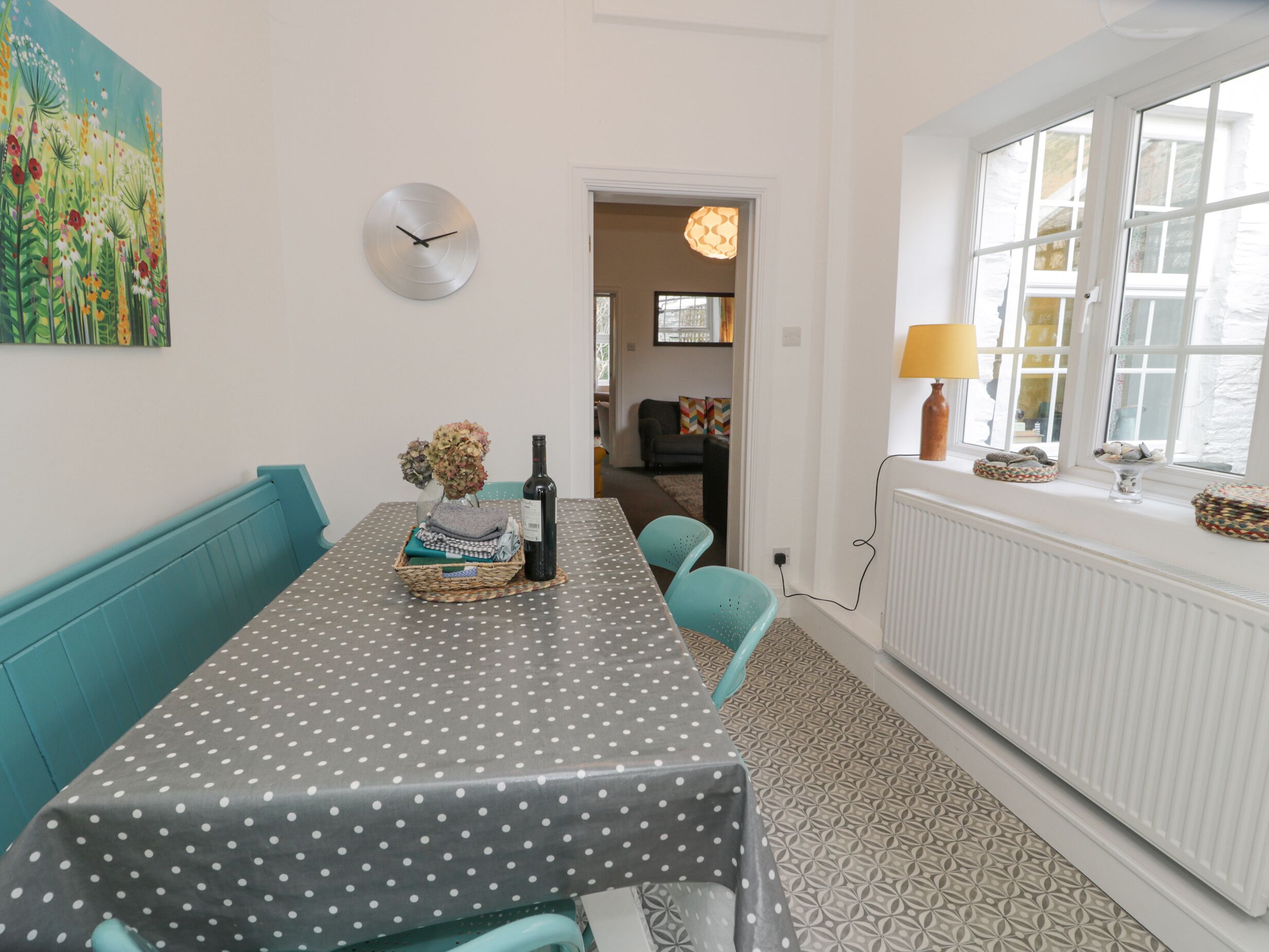 Un coin repas avec une nappe à pois, des chaises de couleur turquoise, une bouteille de vin et un vase de fleurs.