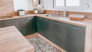 Een moderne keuken met donkere kasten, een houten aanrechtblad, een geïntegreerde spoelbak en een raam met uitzicht op groen.