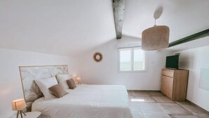 Een slaapkamer met een bed, nachtkastje, lamp en een televisie op een houten kast.