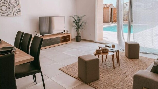 Een moderne woonkamer met een televisie, een eethoek en uitzicht op een zwembad.