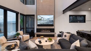 Uma sala de estar moderna com lareira, uma televisão de tela plana grande e um espaço de estar aconchegante com sofá e poltronas.