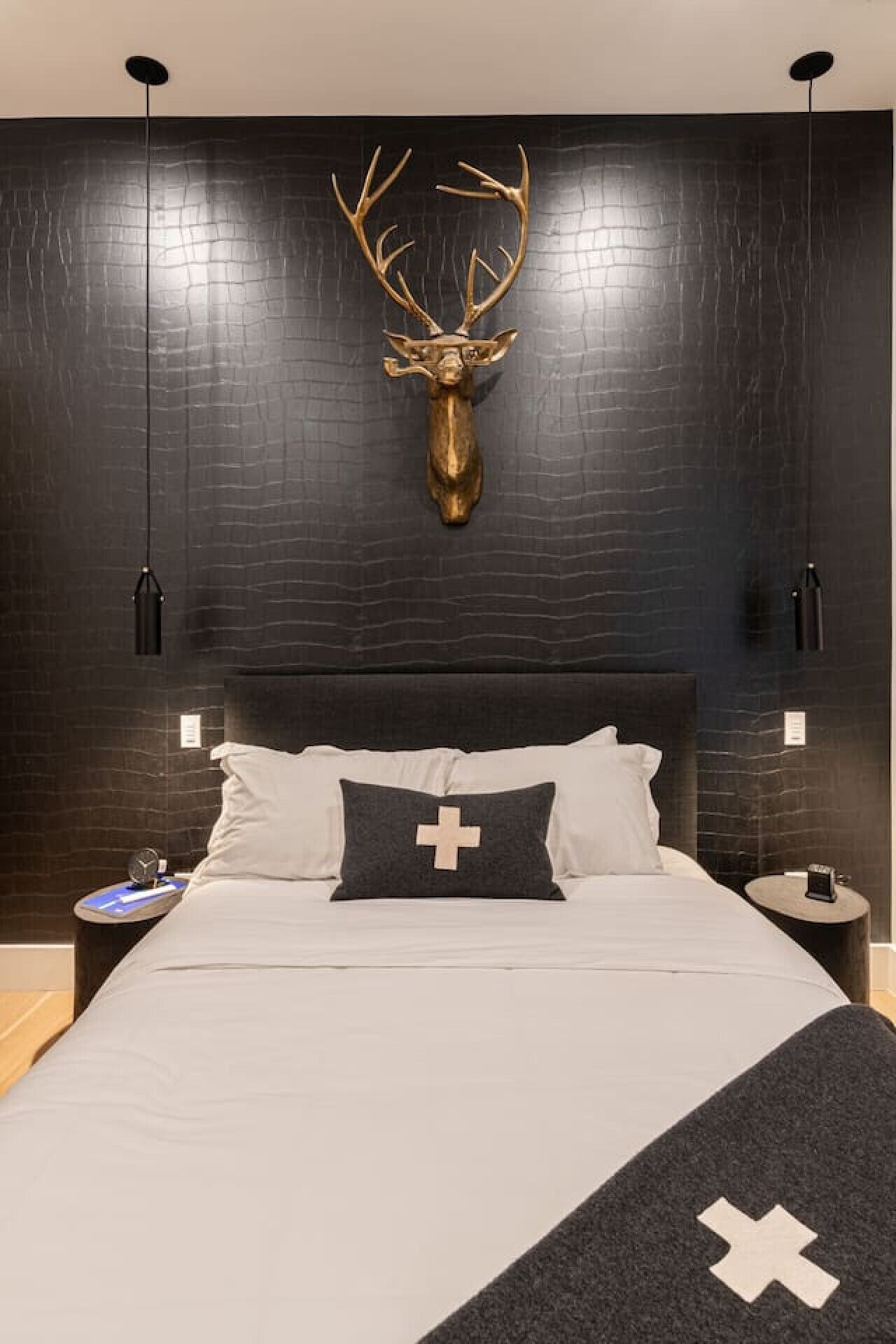 Un dormitorio moderno con una cama grande, dos mesitas de noche, una cabeza de ciervo montada en la pared y una almohada con forma de cruz.