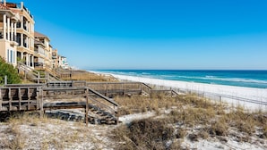 A beachfront property with a wooden boardwalk leading to a sandy beach and ocean.