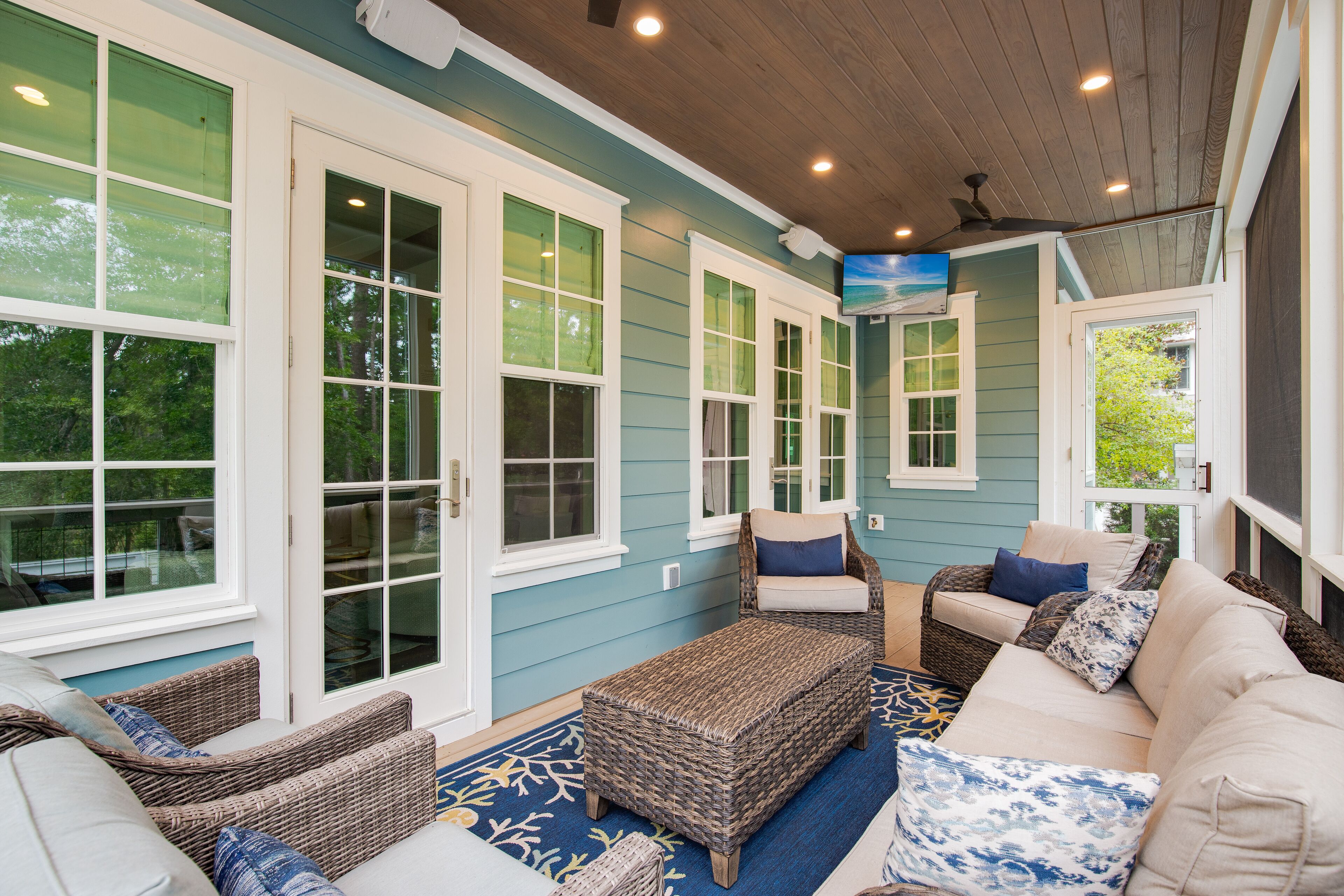 A covered patio area with wicker furniture, large windows, and a ceiling fan.
