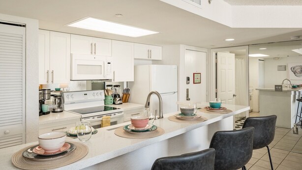 A modern kitchen with white cabinets, a central island with bar seating, and a microwave above the stove. - **THE OSPREY'S NEST** Condo & Pool + Last Key White Glove Service... (Key West)