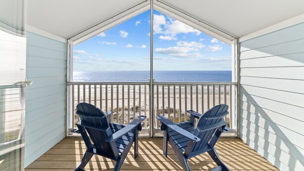 Ein Balkon mit zwei Adirondack-Stühlen mit Blick auf Strand und Meer.