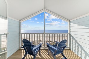 Een balkon met twee Adirondack stoelen, gericht op een strand en zeezicht.