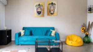 A living room with a blue sofa, a glass coffee table, and a yellow bean bag. There are two paintings on the wall. - Mirador Savoca (Savoca)