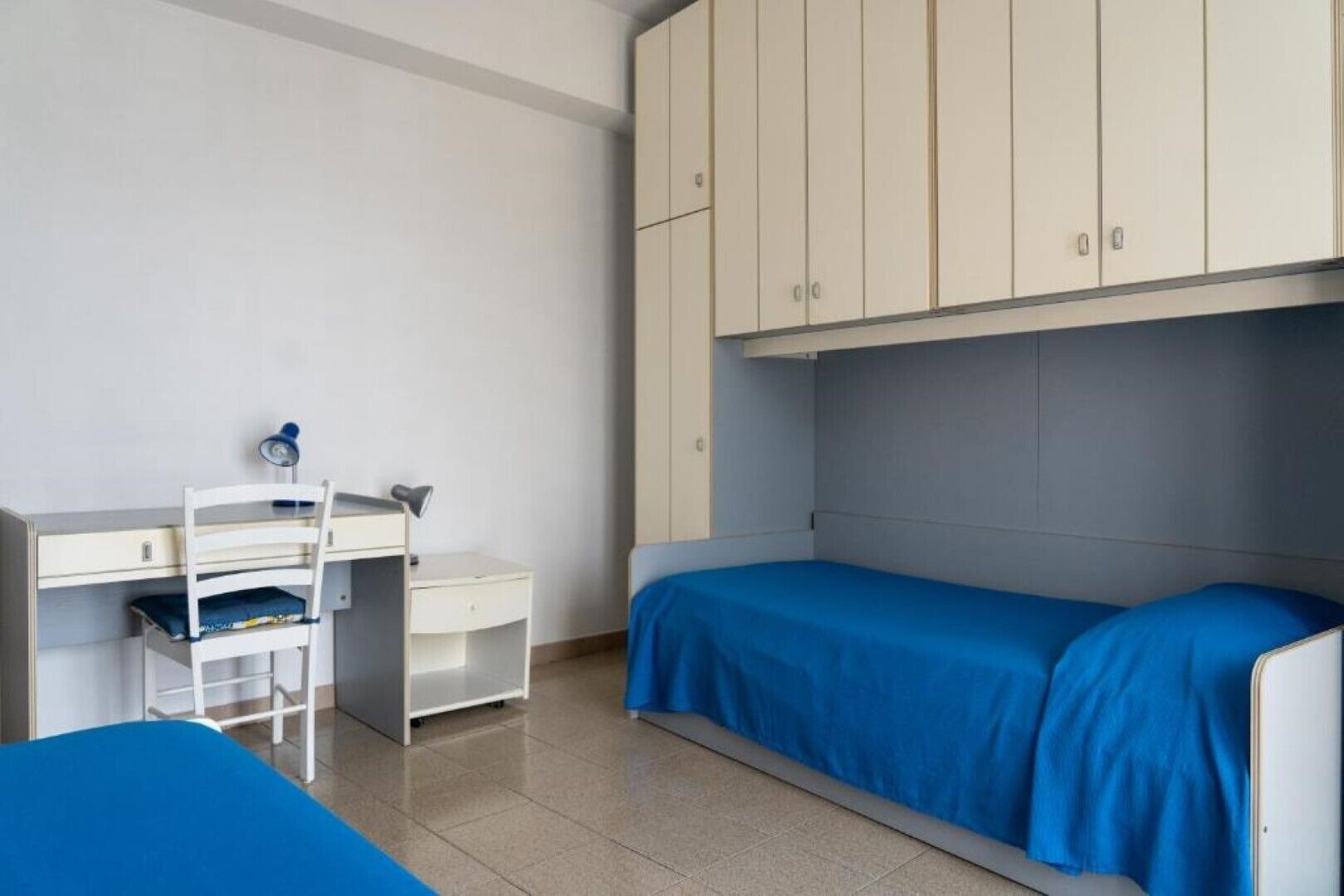 A dormitory room with a bed, a desk, a chair, and a wardrobe.