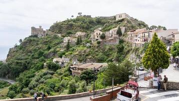 Un poble situat en un turó amb edificis històrics, un camí pavimentat i un vehicle estacionat.
