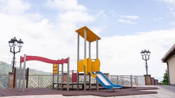 Ein Spielplatz mit Rutsche und Klettergerüst, umgeben von einem Zaun und Straßenlaternen.