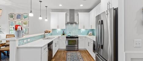 A modern kitchen with white cabinets, a stainless steel refrigerator, and a blue tiled backsplash.