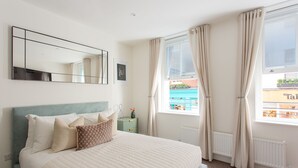 A bedroom with a bed, a bedside table, a mirror, and a window with curtains. - Cosy Gem in Covent Garden (London)