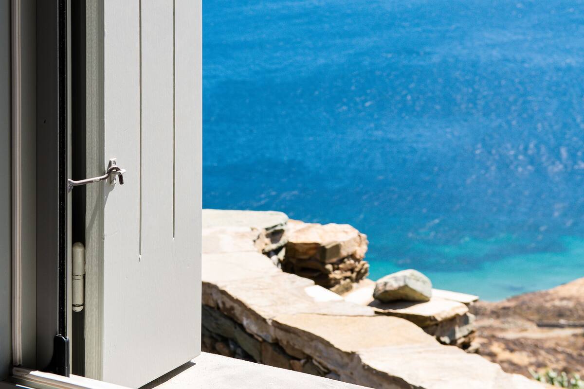 Vista a través de una puerta abierta que da a un balcón con vistas al paisaje costero y montañas a lo lejos.