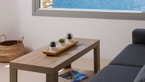 A room with a large window offering a view of the cityscape and mountains, a wooden table with decorative items, a grey sofa, and a hanging light fixture. - Caval Residences (Tinos)