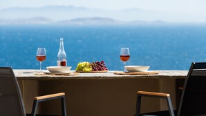 A table set with a bottle, glasses, and a bowl of grapes, overlooking a mountainous landscape. - Caval Residences (Tinos)