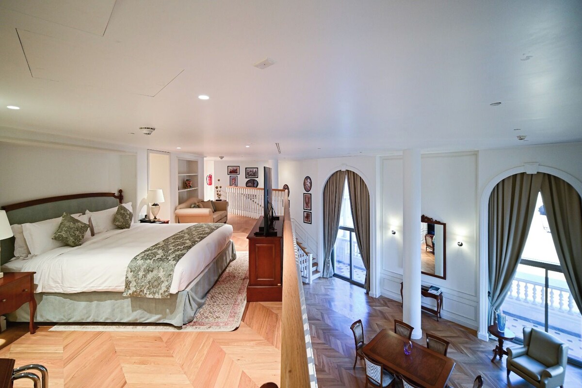 Una camera d'albergo con un letto grande, un'area pranzo con tavolo e sedie e vista sull'esterno.