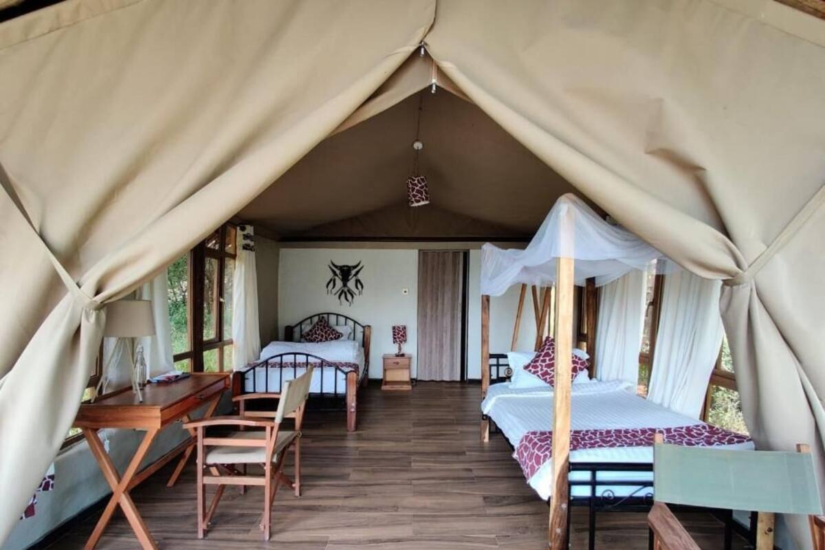 A tented accommodation with a bed, a desk, and chairs.