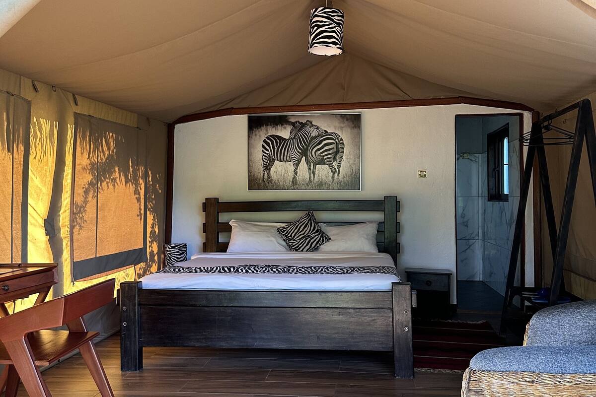 A tented room with a bed, a zebra-themed pillow, and a zebra painting on the wall.